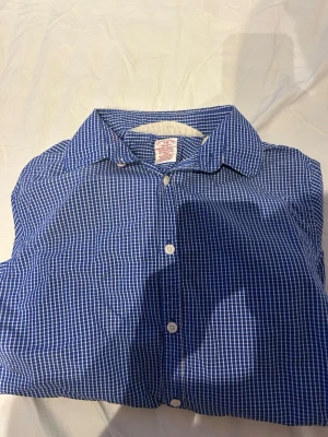 Blårutig skjorta - Klassisk blårutig skjorta med vit knappstängning och lång ärm. Skjortan har en snygg krage och är tillverkad i mjuk bomull, perfekt för en avslappnad men ändå stilren look.