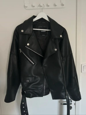 Svart skinnjacka  - Säljer min svarta bikerjacka i skinnimitation från Pull&Bear. Klassisk modell med sned dragkedja, silvriga detaljer och markerad krage. Perfekt både öppen och stängd. Helt ny, endast testad för bilden.  Nypris: 500kr