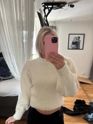 Vit stickad tröja med puffärm - Säljer en krämvit stickad tröja med puffärmar och ribbade muddar. Tröjan har en croppad passform och rund halsringning. Perfekt för dig som gillar en trendig och mysig look. Materialet känns mjukt och tjockt, troligen ullblandning.
