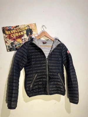 Svart dunjacka från Colmar - Snygg svart dunjacka från Colmar med quiltad design och två dragkedjeförsedda fickor. Jackan har en diskret logga på ärmen och en hög krage. Perfekt för kalla vinterdagar och riktigt lätt att bära.