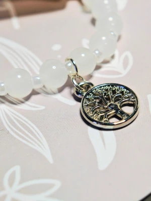 Vitt pärlarmband med livets träd-berlock - Snyggt armband med vita, runda glas pärlor och en silverfärgad berlock i form av livets träd. Armbandet har elastisk tråd för enkel påtagning och passar perfekt för dig som gillar stilrena accessoarer med en symbolisk touch. 18 cm i omkrets 