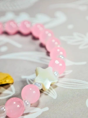 Rosa pärlarmband med stjärndetalj - Sött armband med ljusrosa glaspärlor och små vita pärlor mellan varje. Armbandet har en vit stjärnformad pärla i pärlemor som detalj och mäter 18 cm. Perfekt för dig som gillar gulliga accessoarer och vill addera lite färg till din stil.Elastiskt armband av hög kvalitet.