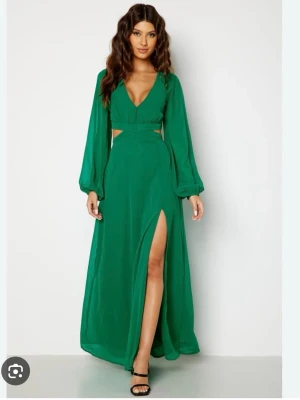 Grön långklänning med slits och knyt - Snygg grön bal/långklänning med v-ringning, långa ärmar och hög slits framtill. Klänningen har öppen rygg med knytband och cut out-detaljer i midjan. Perfekt för dig som vill sticka ut med en trendig och elegant look. !!Aldrig använd!!