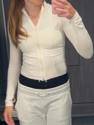 Vit långärmad topp med dragkedja - Säljer en creme vit, långärmad och tight träningsjacka/tröja med dragkedja framtill. Snygg och enkel design som passar till mycket.