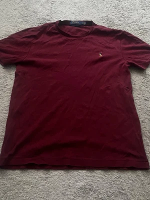 Vinröd t-shirt från Polo Ralph Lauren - Snygg vinröd t-shirt från Polo Ralph Lauren med klassisk rund hals och liten broderad logga på bröstet. Modellen är custom slim fit och tillverkad i mjuk bomull som känns skön mot huden. Perfekt för dig som gillar stilrena plagg med en ikonisk touch.