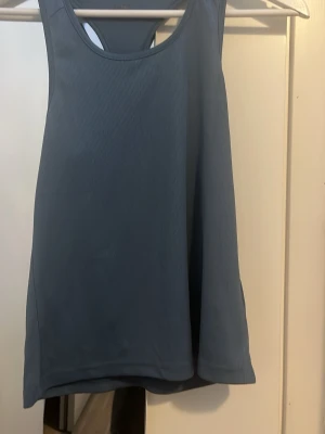 Blå ribbad linnetopp från SATS - Snygg blå linnetopp från SATS i ribbad syntet med sportig look. Perfekt för dig som gillar träning och vill ha ett bekvämt och stilrent linne. Modellen är ärmlös och har en klassisk rund halsringning och brotarygg.