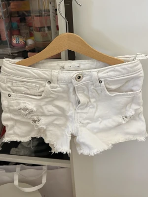 Vita denimshorts från ZARA - Snygga vita denimshorts från ZARA med slitna detaljer och fransig kant. Klassisk femficksmodell med knapp och dragkedja framtill. Perfekta för sommaren och ger en avslappnad look.
