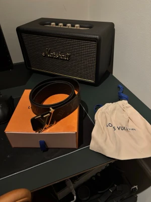 Louis Vuitton brunt skärp med monogram - Snyggt brunt skärp från Louis Vuitton med klassiskt monogrammönster och guldfärgat LV-spänne. Skärpet kommer med originalförpackning och dustbag. Perfekt accessoar för att lyfta din outfit.