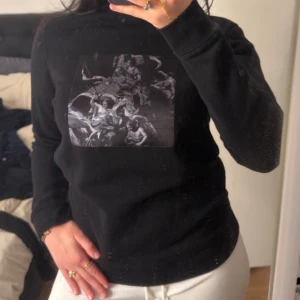 Svart sweatshirt med tryck - Säljer en svart sweatshirt med ett stort grafiskt tryck i gråskala på bröstet. Tröjan har rund halsringning och långa ärmar. Perfekt för dig som gillar streetwear och vill ha en stilren men ändå unik look.