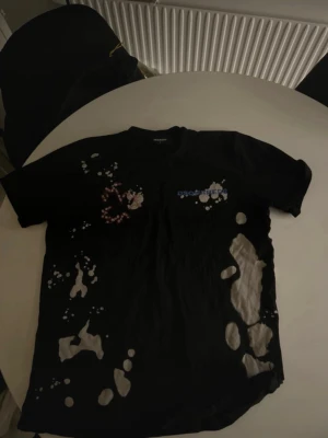 Svart t-shirt med blekta fläckar - Cool svart t-shirt från Represent med unika blekta fläckar och tryck på bröstet. T-shirten har korta ärmar och en relaxed passform, perfekt för dig som gillar streetwear och vill sticka ut lite extra.