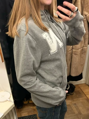 Grå hoodie med brodering/tryck - Grå hoodie med så snygg brodering på bröstet! På storlekstaggen står det XL men skulle säga att det är mer som en oversize M eller L💓 Som referens är jag 175 cm lång💓 Hör av er vid frågor!! 