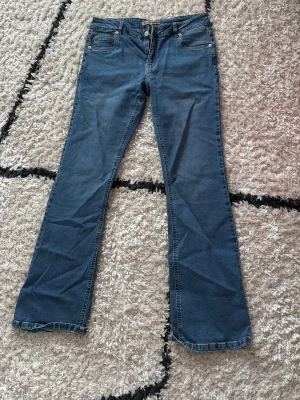 Blå bootcut jeans från Denim Rebel - Säljer ett par klassiska blå bootcut jeans från ullared/gekås! Jeansen har fem fickor, normalhög midja och snygga söm-detaljer. Tillverkade i mjuk denim med dragkedja och knapp framtill. Perfekta för en avslappnad och trendig look. Jag säljer dem för de sitter fel på mig och är för långa. Jag är 161 och är lite mer än 5cm långa på mig! Helt nya! Bara testade!