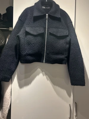 Marinblå jacka  från Zara - Snygg marinblå jacka från Zara med dragkedja framtill och två stora bröstfickor. Jackan har en croppad passform, klassisk krage och är gjord i ett mjukt, fluffigt material som ger en trendig look.