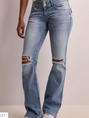 Bootcut jeans - Snygga ljusblå bootcut jeans med slitningar och hål vid knäna. Jeansen har klassisk femficksdesign, dubbla knappar i midjan och fickor med lock bak. Perfekta för en avslappnad och trendig look. nypris är 700 kr