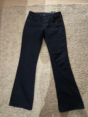 Svarta bootcut jeans - Säljer ett par mörkblåa bootcut jeans med klassisk femficksmodell och utsvängda ben. Jeansen har hög midja och är tillverkade i ett mjukt denimtyg som ger en snygg siluett. 