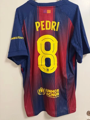FC Barcelona matchtröja Pedri #8 - Snygg FC Barcelona matchtröja från Nike med Pedri och nummer 8 på ryggen. Tröjan har klassiska blå och röda ränder, klubbmärke och Nike-logga på bröstet samt Spotify som sponsor. Tillverkad i lätt och ventilerande material, perfekt för fotboll eller träning.