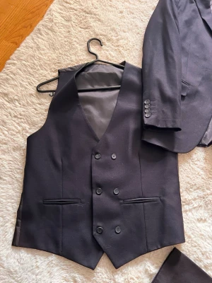 Svarta kostymherr - Snygga svarta kostymbyxor med klassisk rak passform och pressveck. Byxorna har fickor fram och bak, samt bälteshällor. Materialet är slätt och har en elegant finish, perfekt till kavaj och väst för en stilren look.