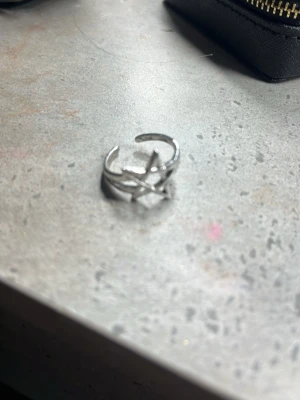 Silverfärgad ring med stjärndesign - Cool ring i silverfärgad metall med öppen design och en stjärnformad detalj framtill. Ringen har en modern och trendig look som sticker ut och passar perfekt för dig som gillar unika accessoarer. Justerbar storlek för bästa passform.