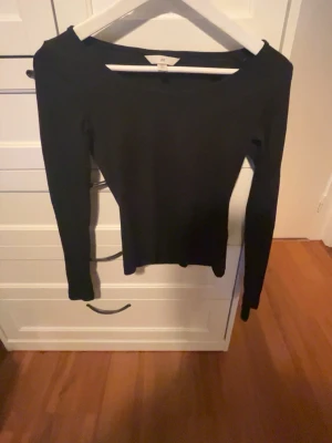 Svart långärmad topp från H&M - En enkel och stilren svart långärmad topp från H&M. Modellen har en något bredare urringning och är figurnära i passformen. Perfekt att matcha med jeans eller kjol för en clean look. Den är stretchig så passar dom flesta
