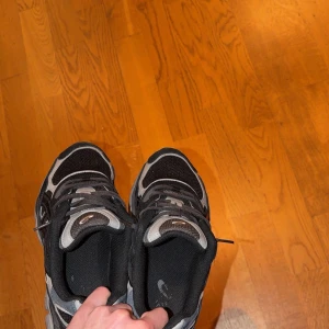 Nike svart/grå sneakers - Säljer ett par svarta och grå Nike sneakers med coola detaljer och klassisk swoosh på sidan. Skorna har mesh och syntetmaterial för bra andningsförmåga och komfort. Perfekta för dig som gillar sportig stil och streetwear. 