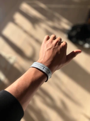 Turkos tygarmband med vit text och detaljer från Dior - Snyggt grått tygarmband från Christian Dior med broderad logga i vitt. Armbandet har justerbar knytning med tofsar i ändarna och en stilren, modern look. Perfekt accessoar för att lyfta din outfit med en exklusiv touch.