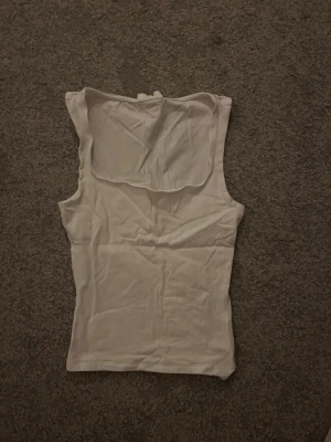 Vit ärmlös linnetopp med krage - Säljer en enkel och stilren vit linnetopp med hög, lös krage. Toppen är ärmlös och har en rak passform som sitter snyggt på kroppen. Perfekt att matcha med jeans eller kjol för en clean look.