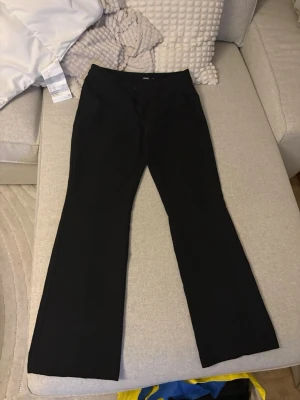 Svarta kostymbyxor från BikBok - Stilrena svarta kostymbyxor från BikBok med klassisk rak passform och lätt utsvängda ben. Byxorna har hällor för skärp och stängs med dragkedja och knapp. Perfekta för en snygg och uppklädd look. Lågmidjade, storlek 40 men väldigt små i storleken skulle säga att de sitter sol S