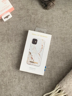 Carrara Gold mobilskal i marmorlook 11/XR (oöppnad förpackning) - Snyggt mobilskal från iDeal of Sweden i modellen Carrara Gold. Skalets design har vit marmoreffekt med guldiga detaljer och en liten guldfärgad logotyp. Passar till iPhone. Tillverkat i slitstark plast med lyxig känsla.