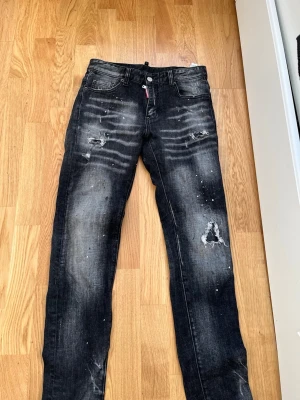 Svarta slitna jeans med hål - Säljer ett par svarta jeans med slitningar, hål och färgstänk för en riktigt cool och avslappnad look. Jeansen har raka ben, klassisk femficksmodell och detaljerade slitningar på både fram- och baksida. Perfekta för dig som gillar streetstyle. de är strl 30 de är knappt använda inga skador eller något sånt 