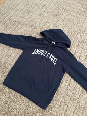 Saint Laurent hoodie - Snygg mörkblå hoodie från Saint laurent som har Amour Cruel med vit text på bröstet. Klassisk känguruficka framtill och justerbar huva med snören. Perfekt för en avslappnad och trendig look. Tillverkad i mjukt bomullsmaterial. helt ny inte ens tagit bort lapparna