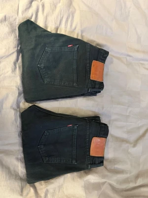 Levis 501 Svarta 30/30 - Säljer ett par svarta jeans från Levi's med klassisk rak passform och femficksdesign. Jeansen har läderpatch bak i midjan och den ikoniska röda Levi's-taggen på bakfickan. Tillverkade i slitstark denim, perfekta för en avslappnad och tidlös stil.