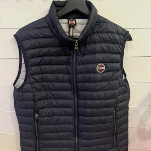 Mörkblå  dunväst från Colmar - Snygg svart dunväst från Colmar med quiltad design och hög krage. Västen har två praktiska fickor med dragkedja och ett Colmar-märke på bröstet. Perfekt att slänga över en hoodie för extra värme. Stängs med dragkedja framtill.