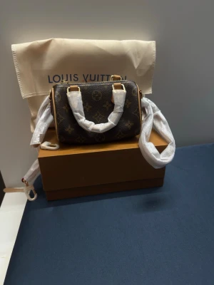  Monogram mini handväska  - Säljer en brun minihandväska  med klassiskt monogrammönster och beige detaljer. Väskan har två korta handtag och avtagbar axelrem i läder. Kommer med dustbag och box. Perfekt accessoar för dig som gillar lyxig och tidlös design.