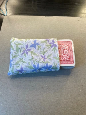 Blommig tygpåse för kortlek - Söt liten tygpåse i vitt med lila och gröna blommor, perfekt för att förvara en kortlek eller småprylar. Påsen är mjuk och har en enkel öppning utan stängning. Passar dig som gillar unika accessoarer med retrovibbar. Bredd 8cm, höjd ca 10 cm. Handgjord med symaskin. För enkel kortlek