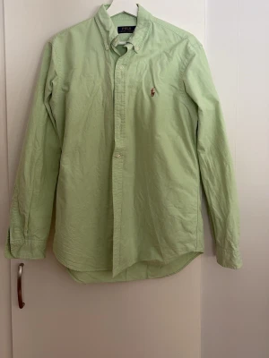 Ljusgrön skjorta från Polo Ralph Lauren - Snygg ljusgrön skjorta från Polo Ralph Lauren med klassisk button-down krage och broderad logga på bröstet. Skjortan har lång ärm och knäppning framtill. Perfekt för en clean och stilren look. Jag är 190 cm och skjortan passar bra på mig.
