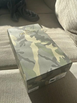 Valentino Garavani sneakers - Snygga sneakers från Valentino Garavani. Kommer i en grön och beige kamouflagemönstrad box med matchande dustbag och extra svarta skosnören. Perfekt för dig som gillar exklusiva och trendiga detaljer från ett välkänt designerbrand.