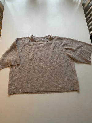 Beige stickad tröja med halvlånga ärmar - Mysig beige stickad tröja med halvlånga ärmar och rund halsringning. Tröjan har en avslappnad, boxig passform och är tillverkad i ett mjukt material som känns skönt mot huden. Perfekt för lager på lager och enkel att styla till olika outfits.