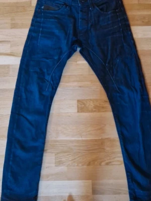 Mörkblå jeans från Jack & Jones - Säljer ett par mörkblå jeans från Jack & Jones med klassisk femficksmodell och raka ben. Jeansen har kontrastsömmar och är tillverkade i ett slitstarkt denimtyg. Perfekta för en avslappnad och trendig stil.