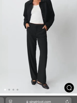 Svarta kostymbyxor från Gina Tricot - Snygga svarta kostymbyxor från Gina Tricot med rak passform och normal midja. Byxorna har pressveck framtill och är tillverkade i ett mjukt, vävt material som ger en clean look. Perfekta att styla med kavaj eller skjorta för en trendig outfit.