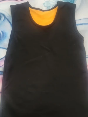 🔥Varm🔥 svart ärmlös linnetopp  -  Vram svart linnetopp med rund halsringning och ärmlös design. Toppen har en slät och enkel form, perfekt för att matcha med olika outfits. Materialet känns mjukt och stretchigt, vilket gör den bekväm att bära. Insidan har en kontrastfärg i gult som ger en cool detalj.Perfekt för kalla dagar när du vill hålla dig varm och bekväm.