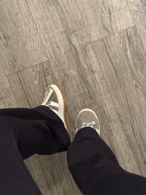 Grå Adidas Campus 00s - Säljer ett par grå Adidas Campus sneakers med klassiska vita ränder på sidan och vit sula med gummidetalj. Skorna har en låg profil och är gjorda i mocka med matchande grå skosnören. Perfekta för en clean och stilren look.