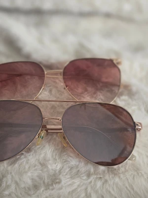 Två par solglasögon guldfärgade - Säljer två par snygga aviator solglasögon med guldfärgade metallbågar. Ena paret har bruna glas och det andra har rosa glas. Klassisk pilotform som ger en cool vibe till din outfit.