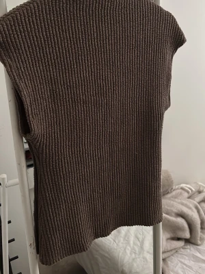 Brun ribbstickad väst Gina Tricot - Brun ribbstickad väst från Gina Tricot med hög krage och ärmlös design. Perfekt att styla över en skjorta eller långärmad tröja. Mjuk och skön kvalitet som ger en trendig look.