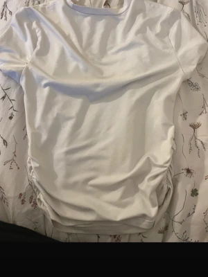 Vit t-shirt med snörning i sidan - Säljer en vit t-shirt med korta ärmar och rund hals. T-shirten har snygg snörningsdetalj i sidorna som ger en trendig look. Perfekt basplagg att styla till olika outfits.