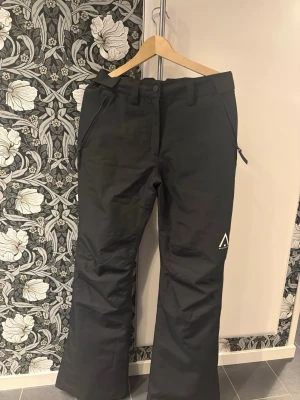 Svarta täckbyxor från wearcolour - Säljer ett par svarta täckbyxor från wearcolour med raka ben, dragkedjor vid fickorna. Byxorna har bälteshällor och diskret logga på ena benet. Perfekta för vinterns alla äventyr i snön. Inte använda mer än 2 gånger så nästan helt oanvända. Har jättefin passform och sitter fint på kroppen.