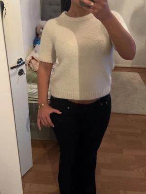 Vit stickad kortärmad topp - Säljer en vit stickad topp med korta ärmar och rund hals. Toppen har en croppad passform och ribbade kanter vid ärmslut och nederkant. Perfekt att styla med både jeans och kjol för en trendig look.