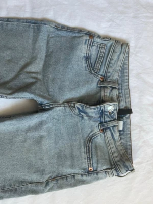 Ljusblå jeans från H&M Divided - Säljer ett par ljusblå mom jeans från H&M Divided. Klassisk femficksmodell med låg midja och utsvängda. Jeansen har snygga kopparfärgade litar och är gjorda i bomull med en vintage tvättad look.