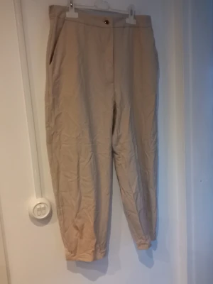 Beige chinos från Zara, storlek L - Snygga beige chinos från Zara i storlek L. Klassisk rak passform med sidofickor och knappstängning i midjan. Tillverkade i ett mjukt och lätt bomullsmaterial som är perfekt för en clean och avslappnad stil.