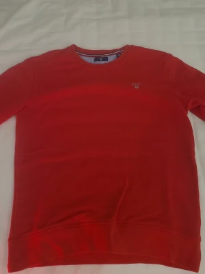 Röd sweatshirt från Gant - Riktigt snygg röd sweatshirt från Gant med rund halsringning och diskret logga broderad på bröstet. Klassisk passform och mjukt material som känns skönt mot huden. Perfekt till jeans eller över en skjorta för en clean look.