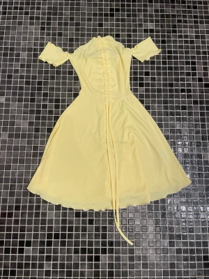 Ljusgul omlottklänning med snörning - Söt ljusgul klänning med offshoulder-ärmar och snörning framtill. Klänningen har en omlott-design och lätt utsvängd kjol som ger en feminin siluett. Perfekt för sommarens alla tillfällen.